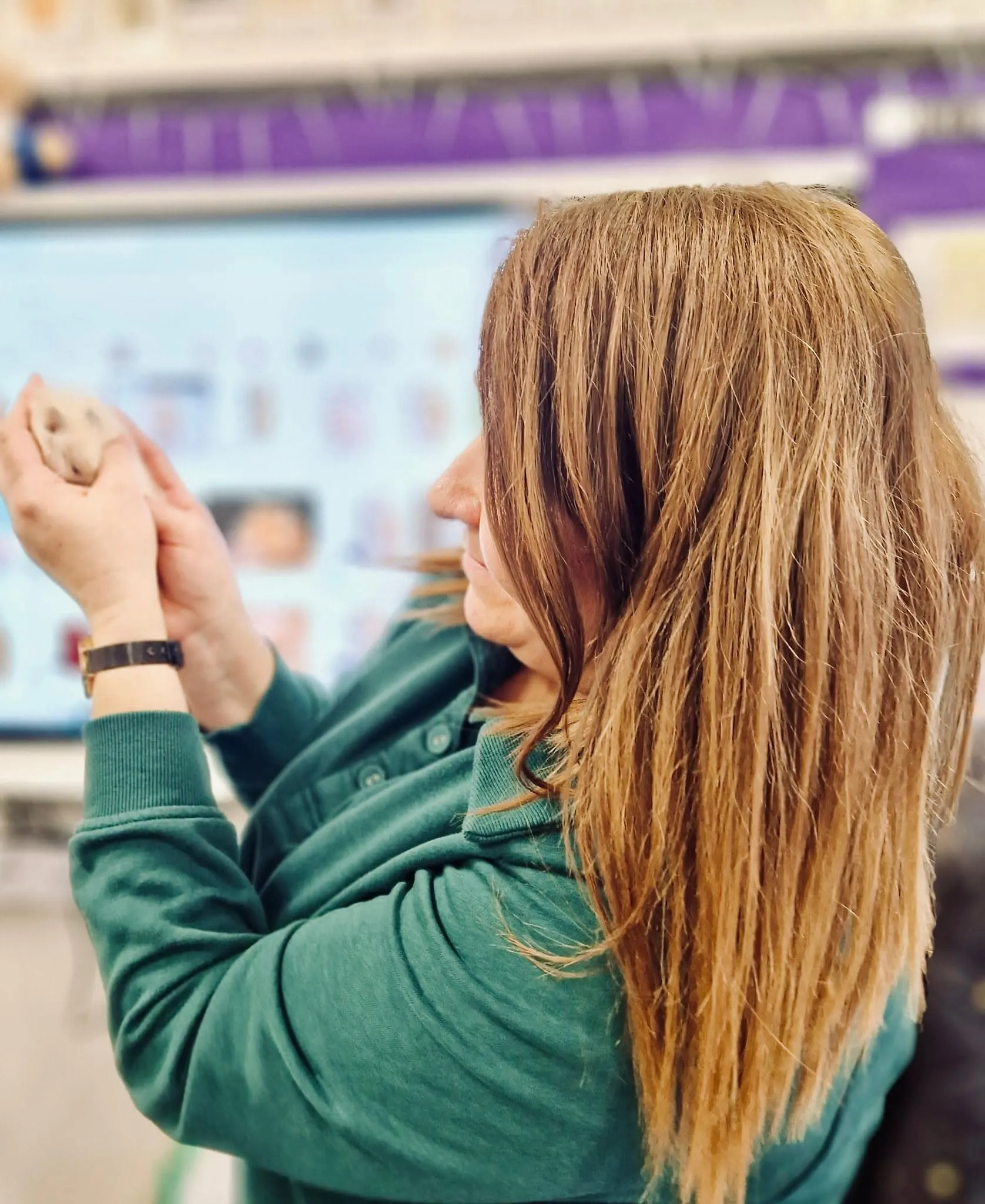 The teacher, seen from behind, shows Coco the hamster to the class, holding it up in front of the interactive whiteboard.
