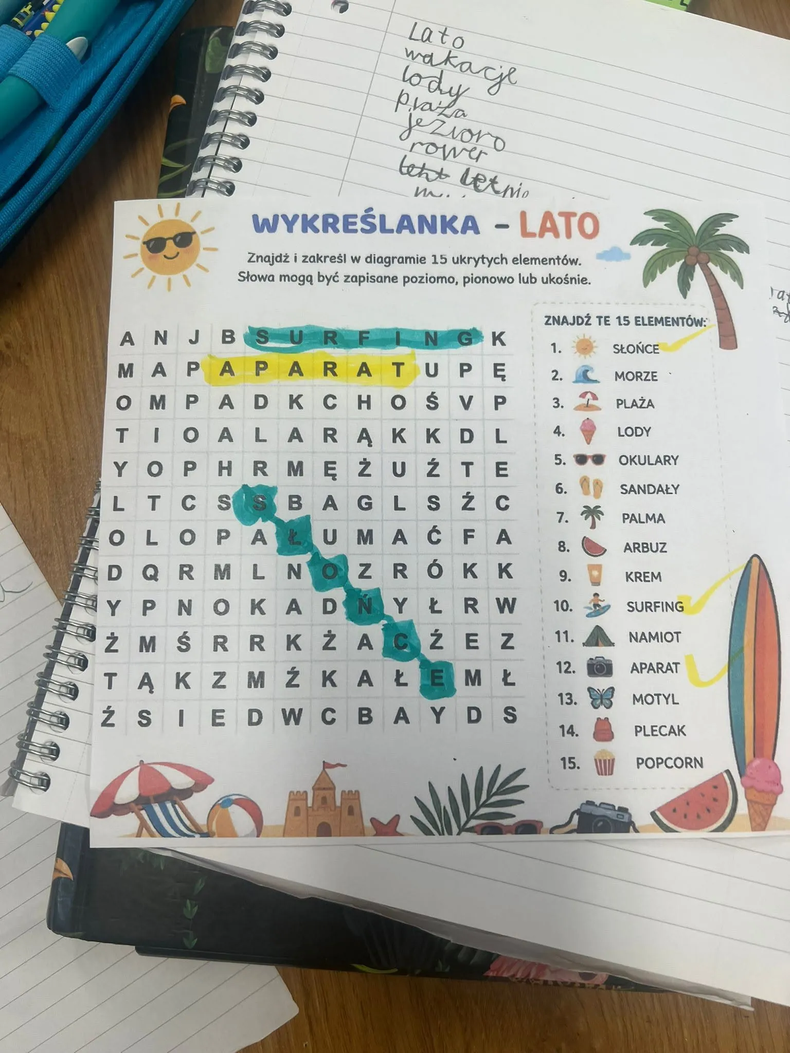 Wykreślanka „Lato” z zaznaczonymi wyrazami, m.in. „aparat”, wklejona do zeszytu obok listy letnich słów.