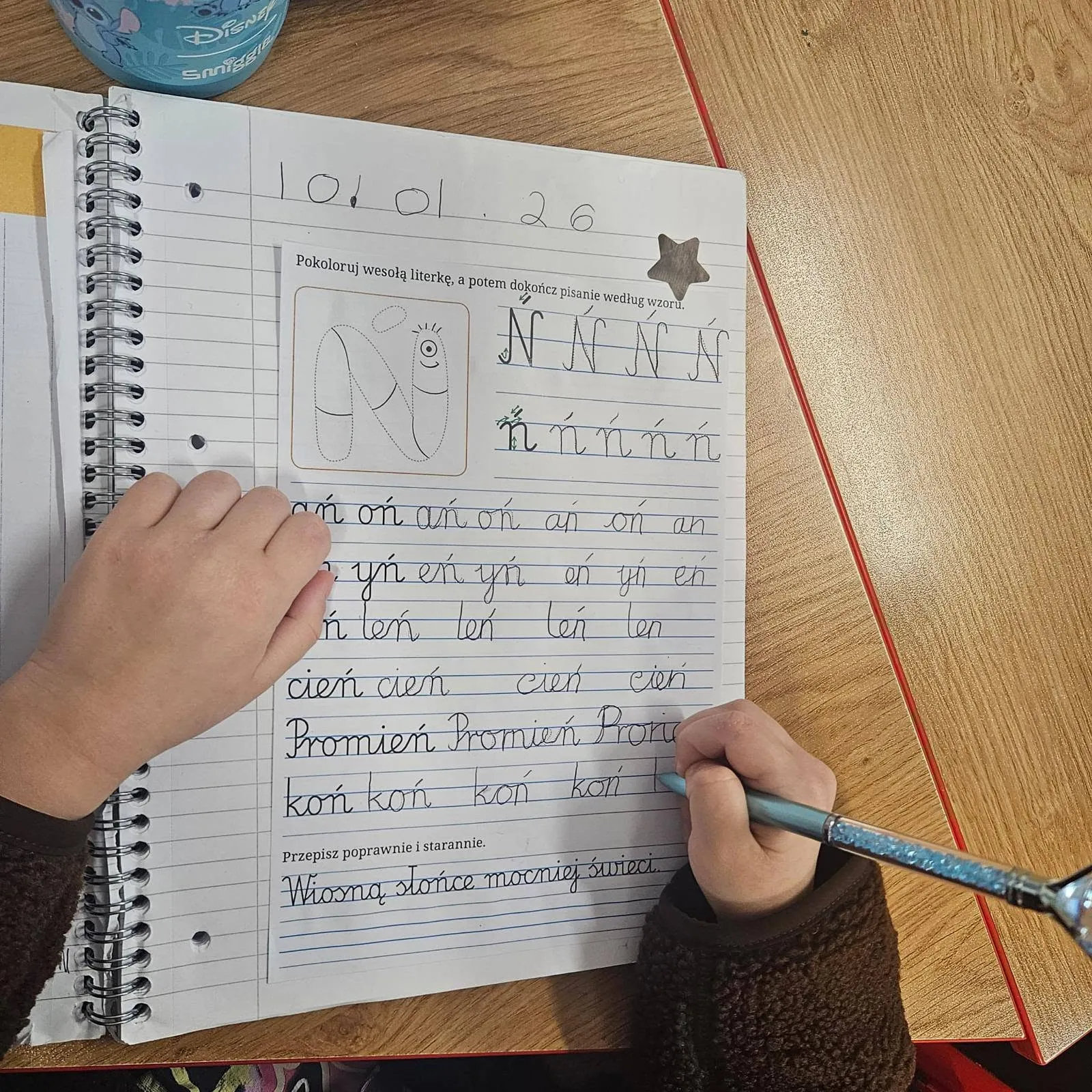 A child's hand practising the Polish letter ń in an exercise book