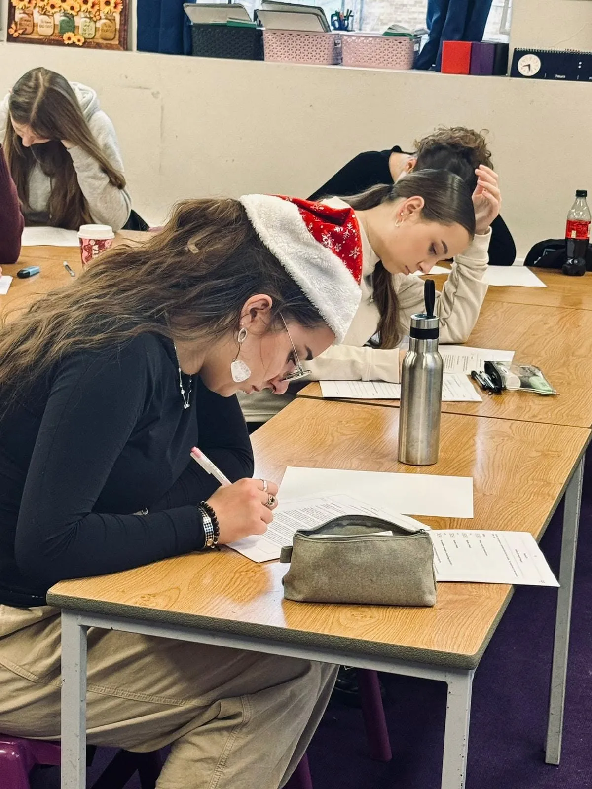 Uczniowie klasy A-level piszą próbny egzamin przy ławkach; jedna z uczennic ma na głowie czapkę Mikołaja.