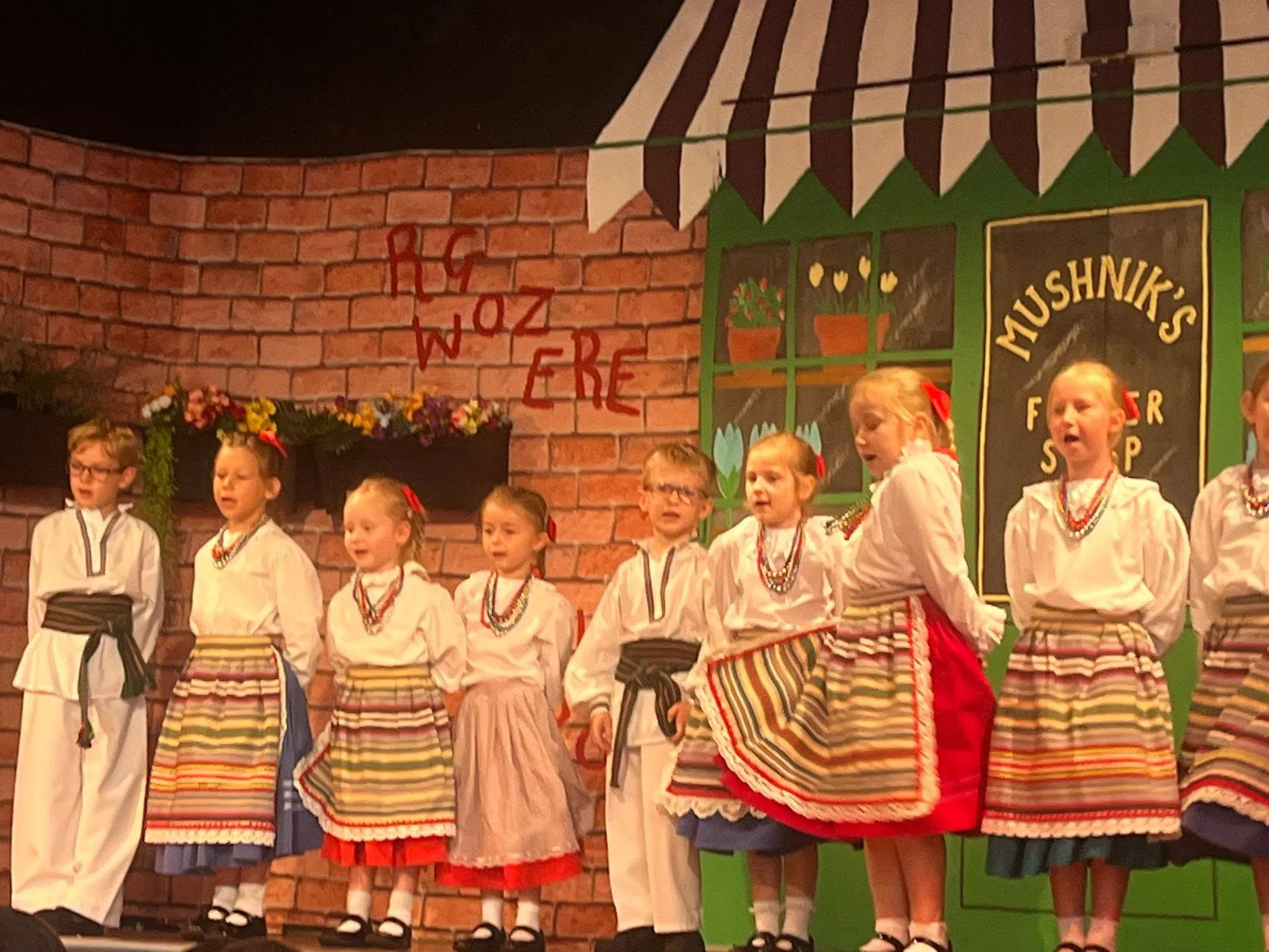 Dzieci w polskich strojach ludowych występują na scenie podczas szkolnego przedstawienia